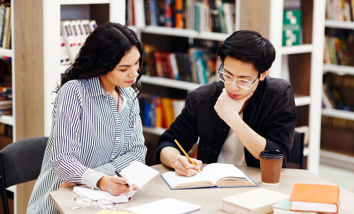 Dos estudiantes concentrados estudiando en una biblioteca.