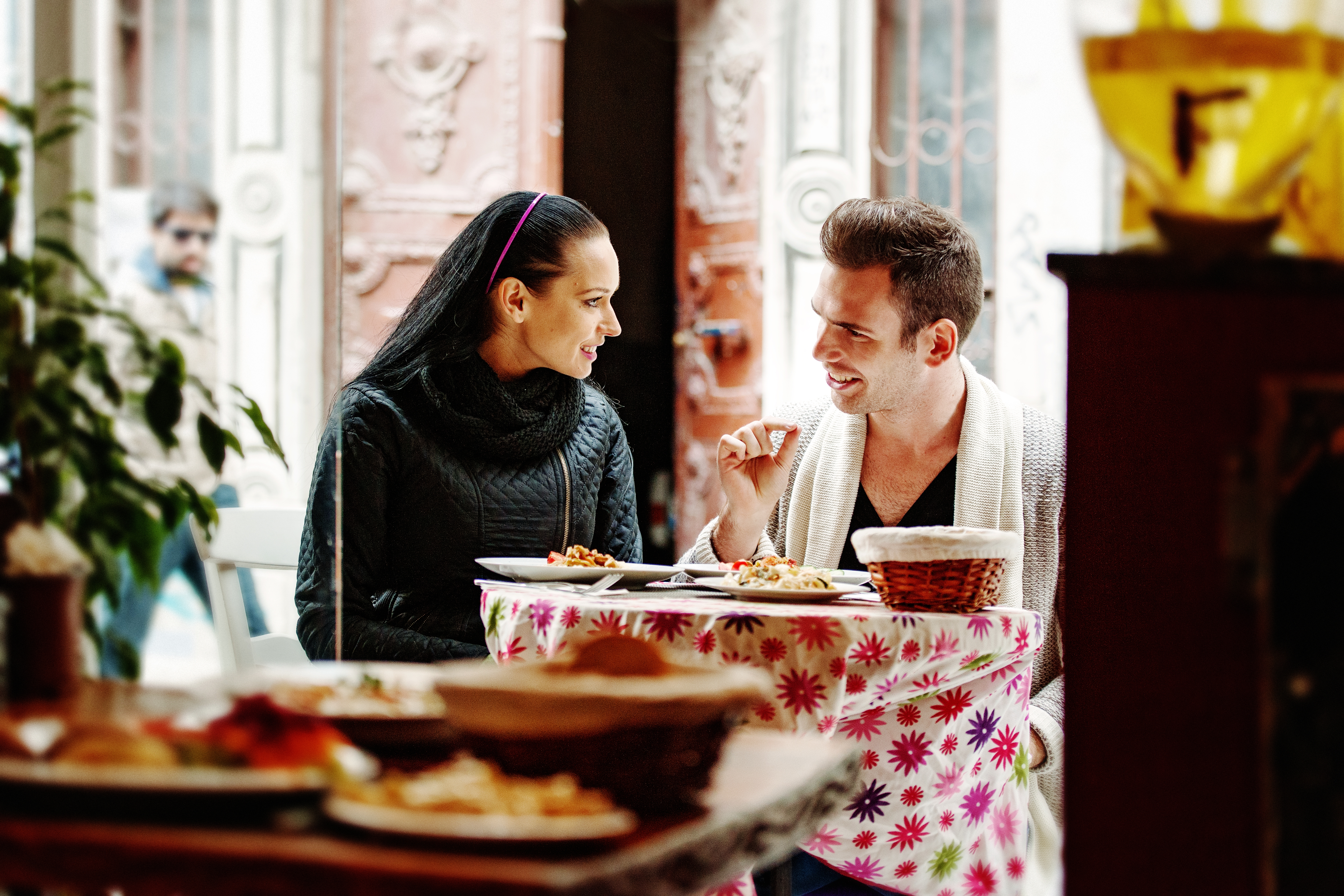 Una pareja joven conversa y sonríe mientras cena al aire libre en un restaurante.