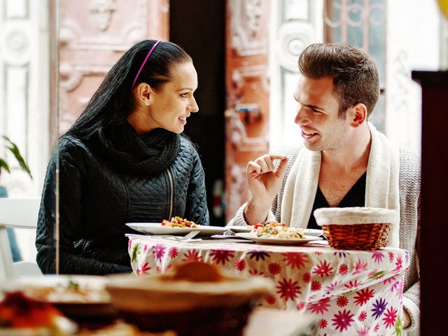Una pareja joven conversa y sonríe mientras cena al aire libre en un restaurante.