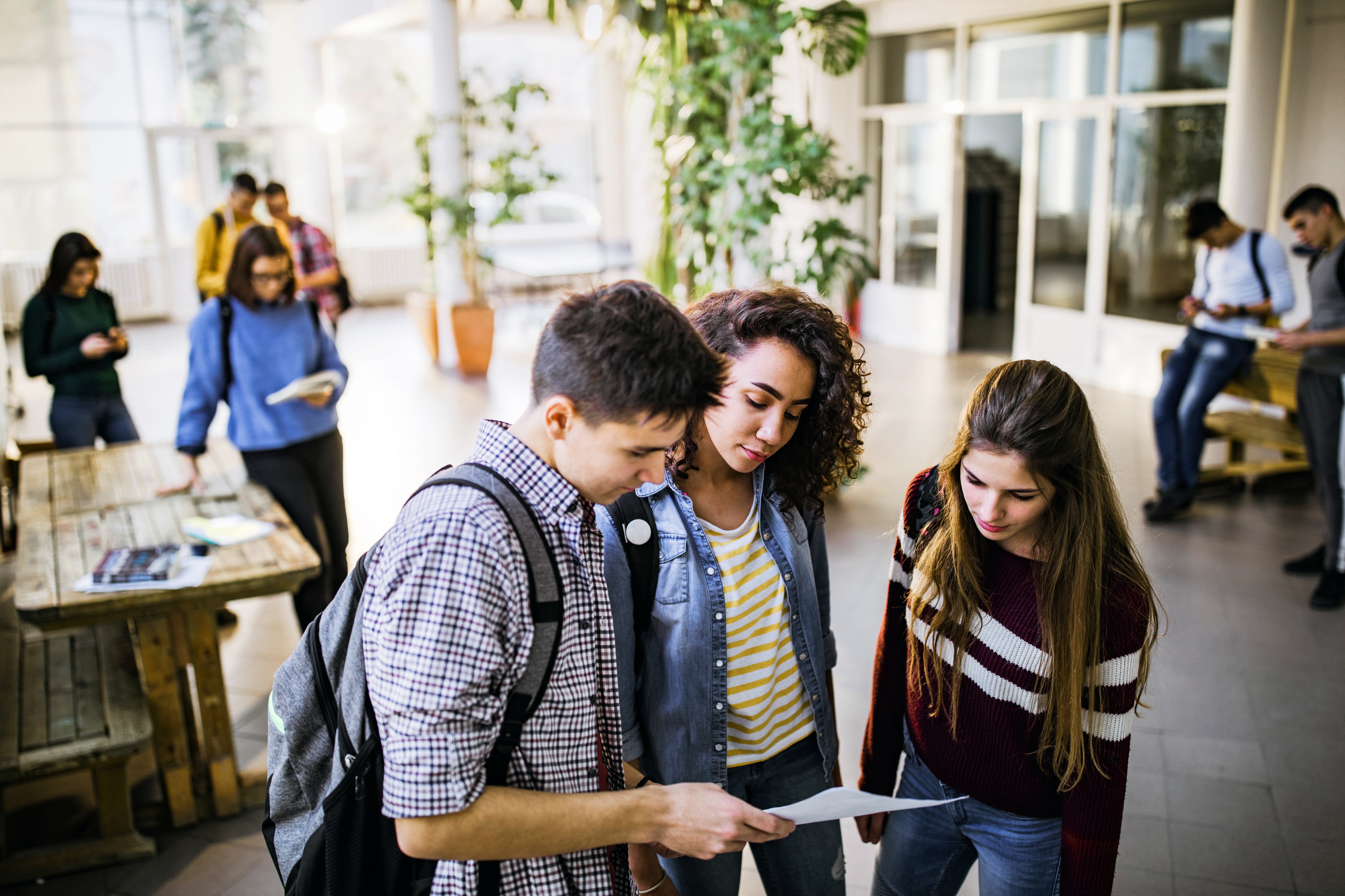 Tres estudiantes revisan papeles juntos en un pasillo concurrido de la universidad.