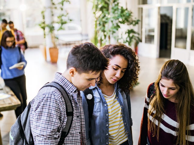 Tres estudiantes revisan papeles juntos en un pasillo concurrido de la universidad.