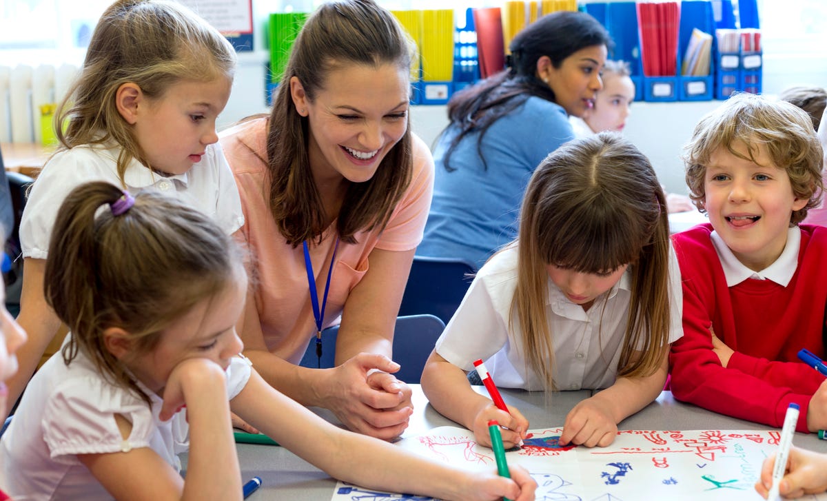Una maestra supervisa y ayuda a un grupo de niños que dibujan y se divierten en clase.