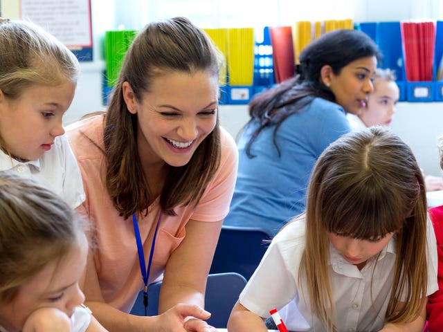 Una maestra supervisa y ayuda a un grupo de niños que dibujan y se divierten en clase.