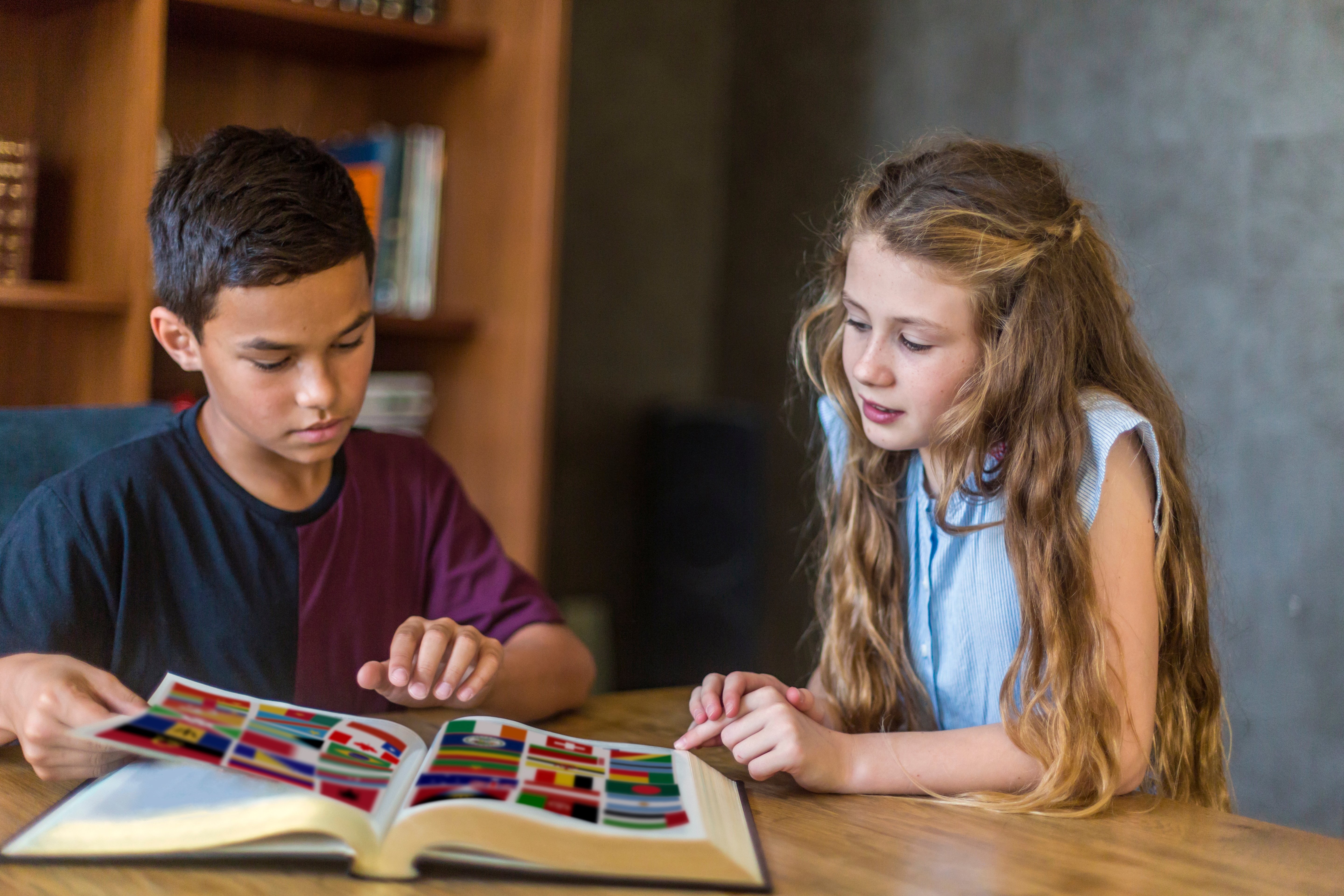 Dos niños exploran un libro de banderas del mundo, aprendiendo juntos.