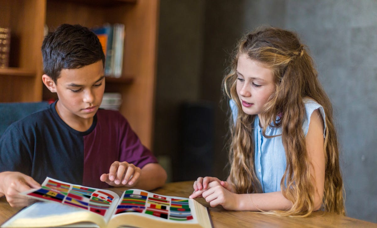 Dos niños exploran un libro de banderas del mundo, aprendiendo juntos.