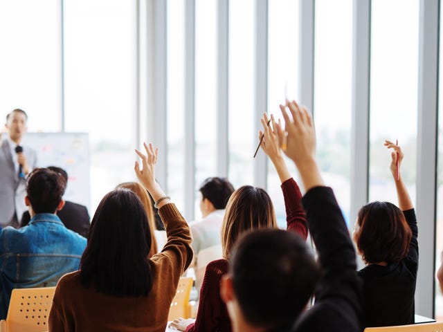 Un profesor se dirige a un grupo de personas que levantan la mano para participar.