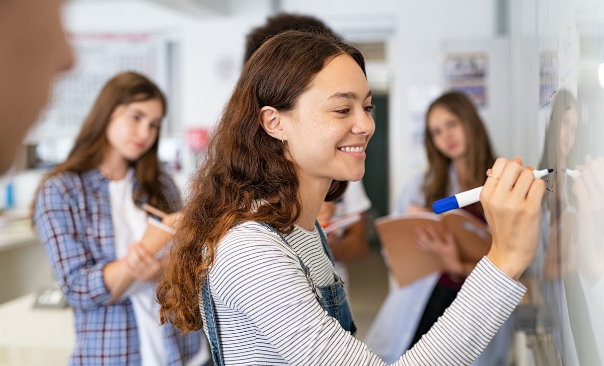 Joven estudiante sonríe escribiendo en pizarra en clase de idiomas Berlitz.