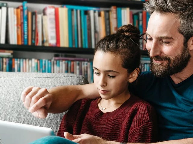 Un padre y su hija sentados juntos en el sofá, compartiendo un momento con una tablet.