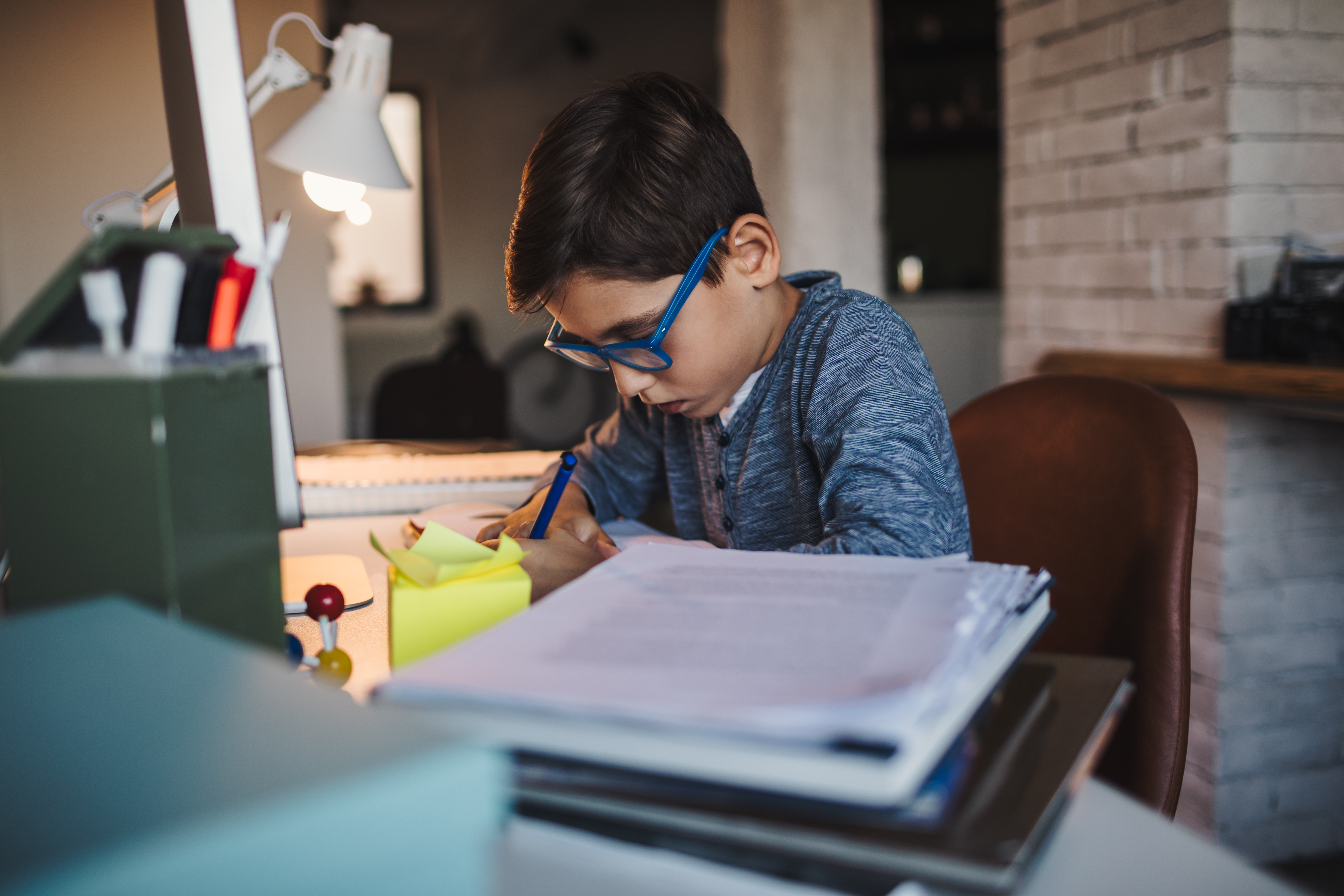 Un niño concentrado haciendo su tarea en el escritorio bajo la luz de una lámpara.