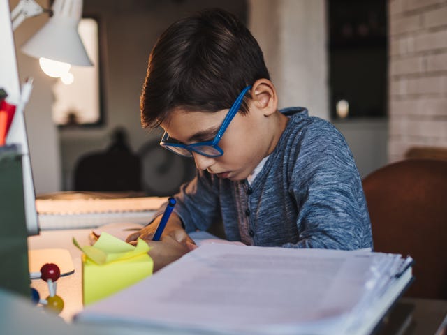 Un niño concentrado haciendo su tarea en el escritorio bajo la luz de una lámpara.