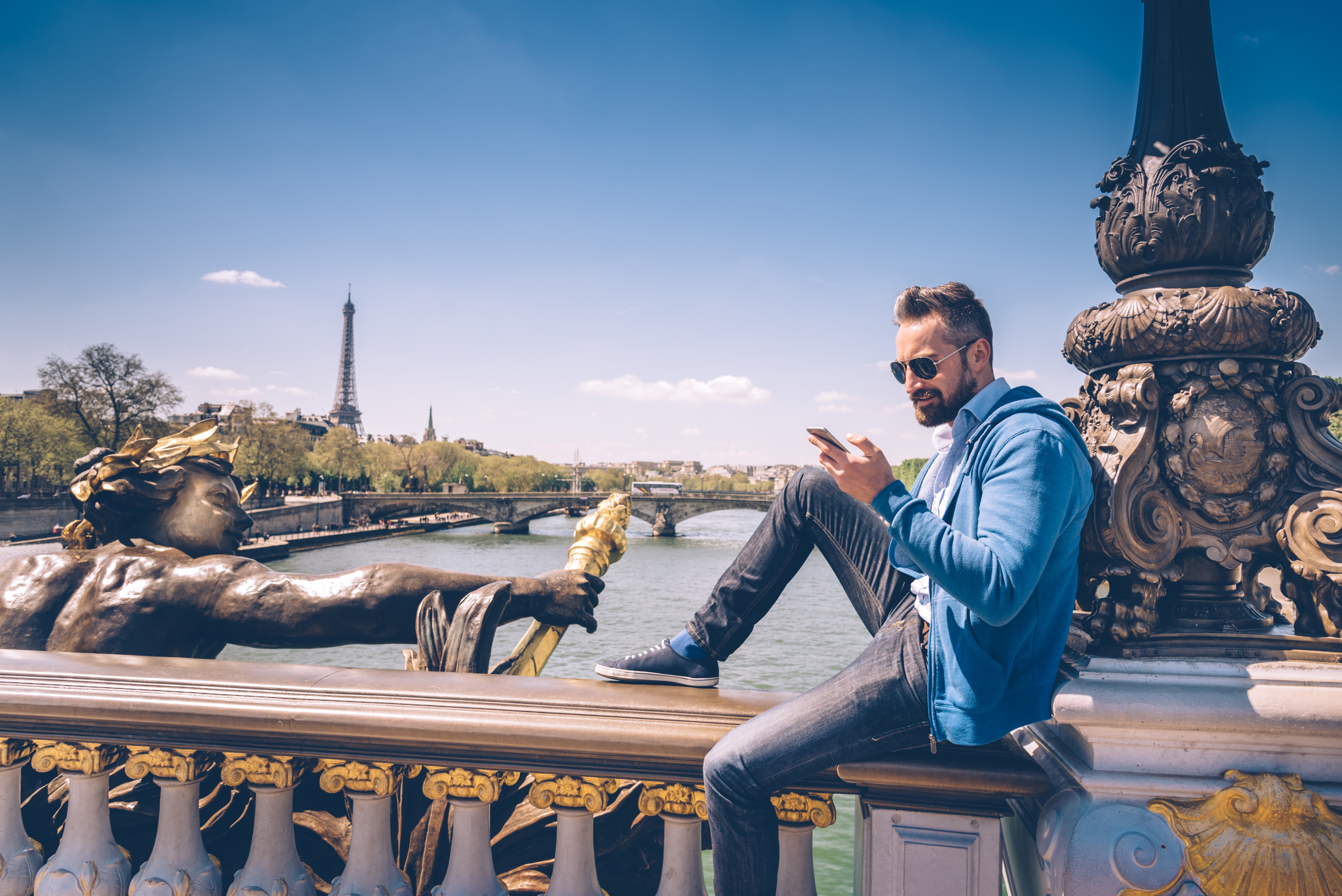 Un hombre con estilo revisa su celular en un puente de París.