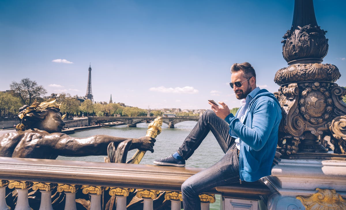 Un hombre con estilo revisa su celular en un puente de París.