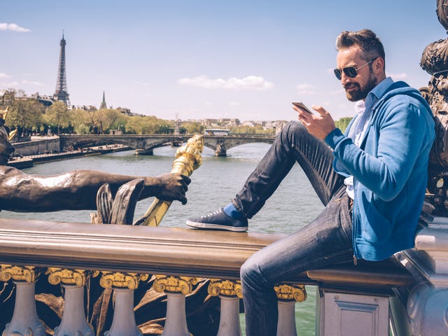 Un hombre con estilo revisa su celular en un puente de París.