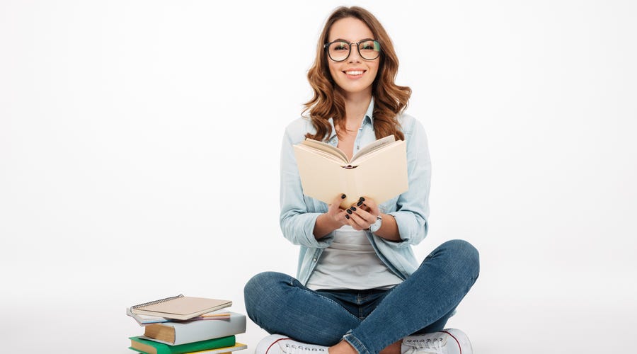 Mujer joven sonríe sentada con libros, estudiando idiomas con Berlitz.