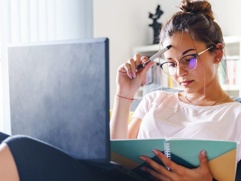 Mujer joven estudia idiomas online Berlitz, concentrada con laptop y libro.