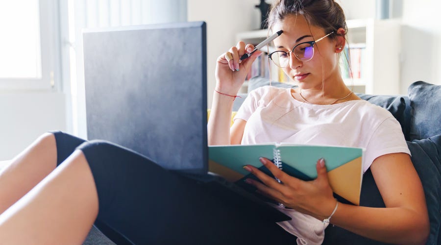 Mujer joven estudia idiomas online Berlitz, concentrada con laptop y libro.