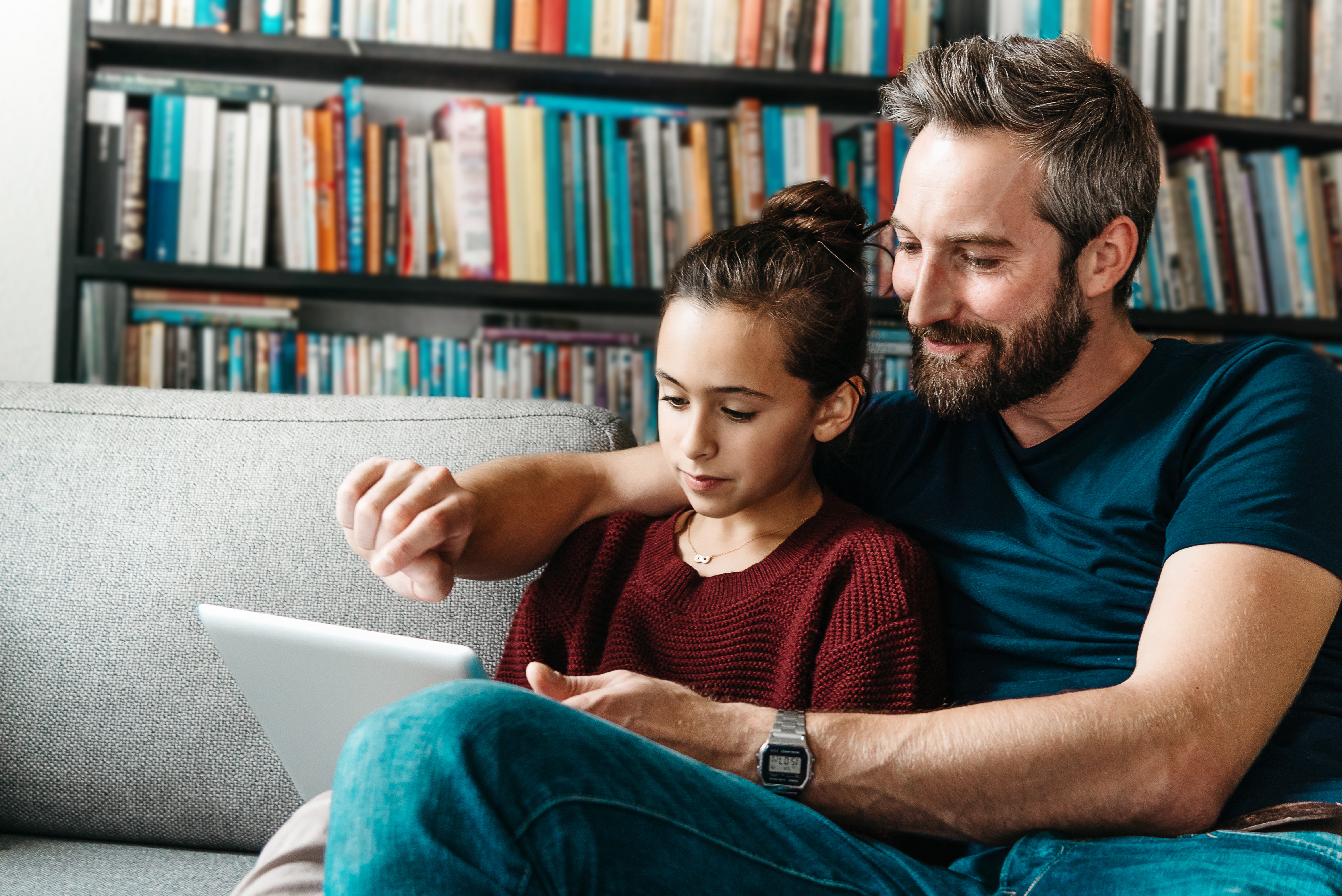 Un padre y su hija sentados juntos en el sofá, compartiendo un momento con una tablet.