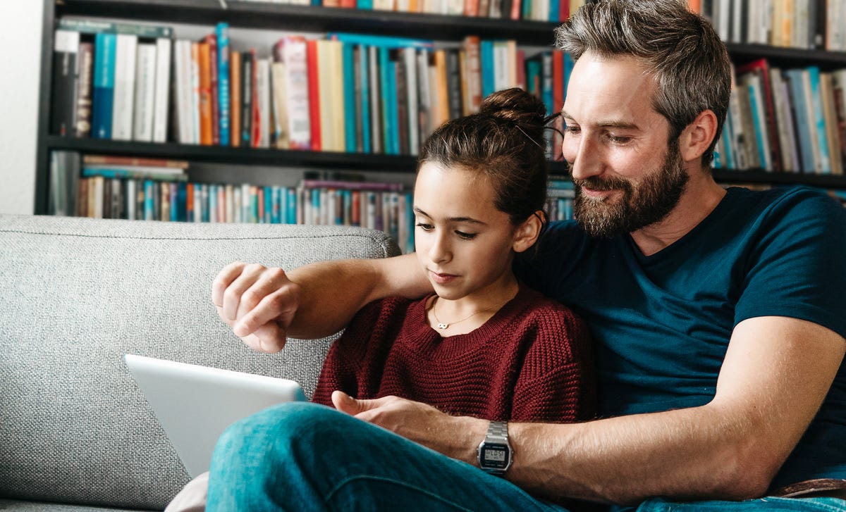Un padre y su hija sentados juntos en el sofá, compartiendo un momento con una tablet.