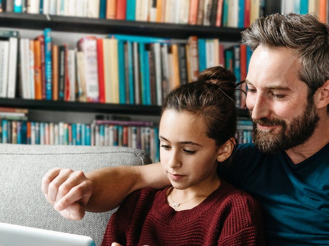 Un padre y su hija sentados juntos en el sofá, compartiendo un momento con una tablet.
