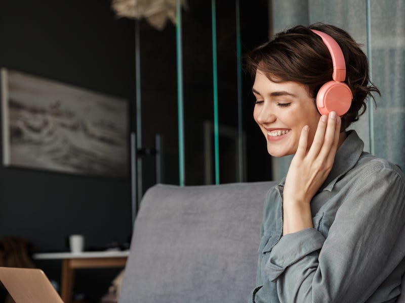 Mujer joven con auriculares aprende idiomas online Berlitz en laptop, sonriendo.