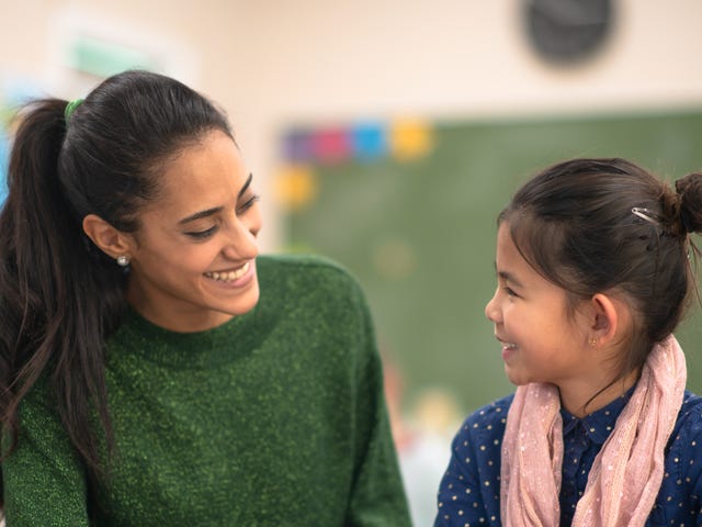 Una maestra joven guía y sonríe a una alumna, trabajando juntas en la clase.