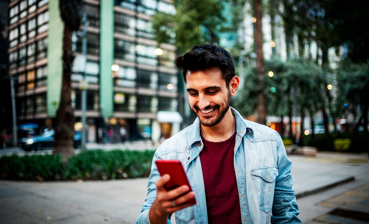 Un joven mira su teléfono celular mientras camina por la calle en una ciudad.