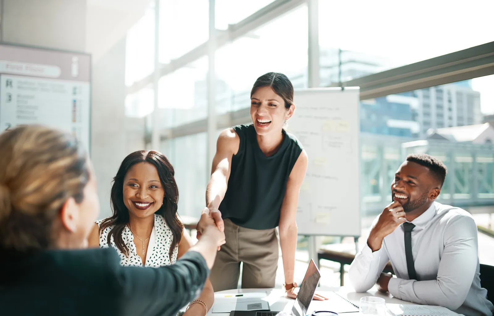 Una mujer de negocios sonriente saluda con un apretón de manos a una colega en una reunión.