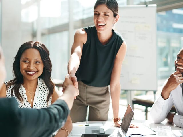 Una mujer de negocios sonriente saluda con un apretón de manos a una colega en una reunión.