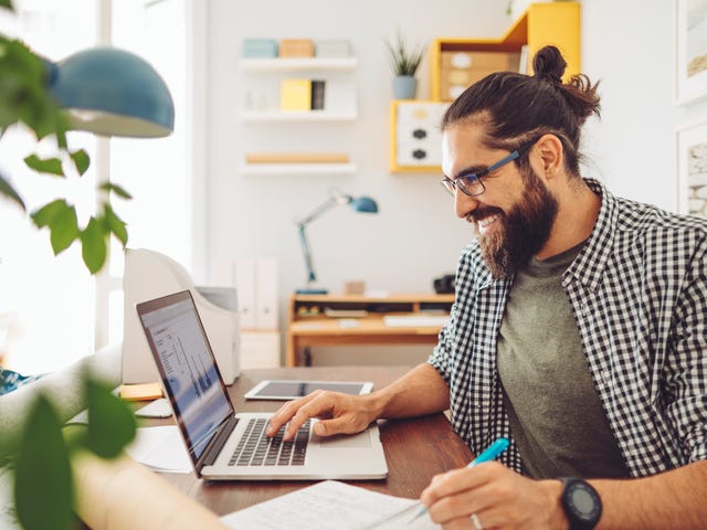 Profesional sonriendo, estudia idiomas online Berlitz con laptop.