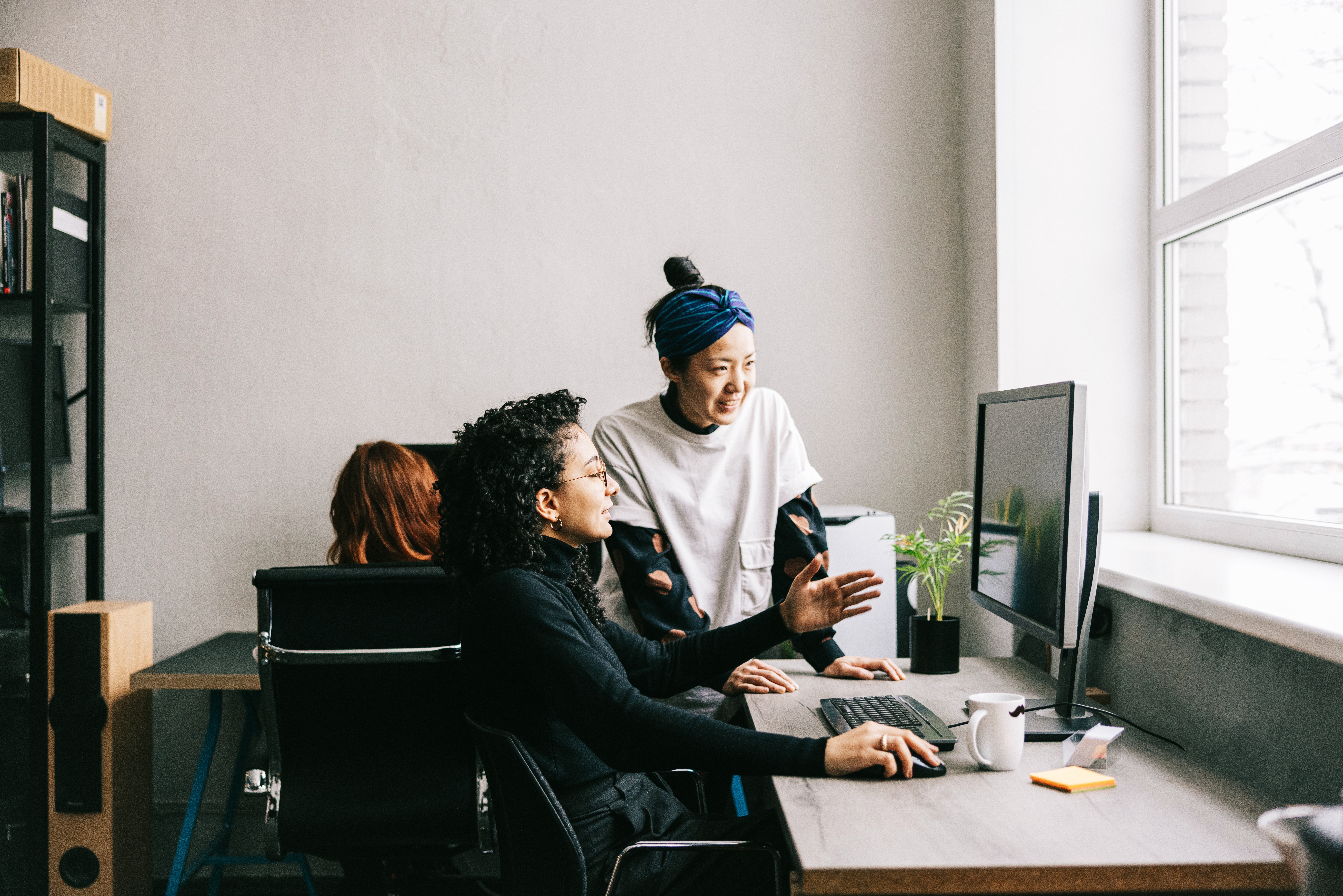 Dos mujeres colaboran y comparten ideas frente a la computadora en una oficina o espacio de trabajo.