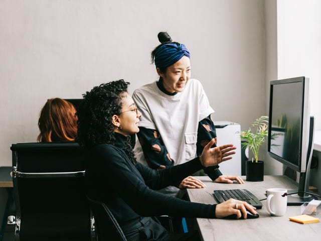 Dos mujeres colaboran y comparten ideas frente a la computadora en una oficina o espacio de trabajo.