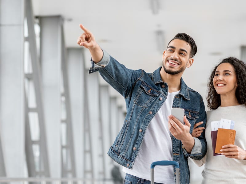 Pareja sonriente con pasaportes en aeropuerto, listos para viajar, gracias a idiomas Berlitz.
