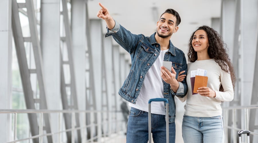 Pareja sonriente con pasaportes en aeropuerto, listos para viajar, gracias a idiomas Berlitz.