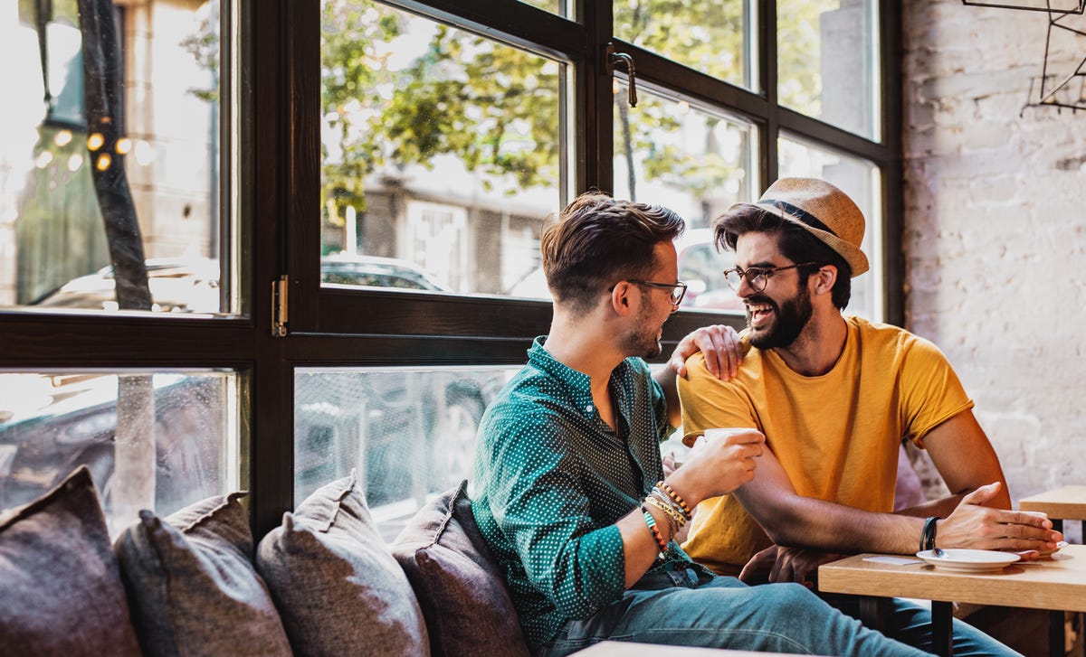 Dos hombres conversan y practican idiomas en cafetería, amigos Berlitz.