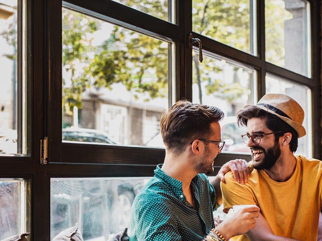 Dos hombres conversan y practican idiomas en cafetería, amigos Berlitz.