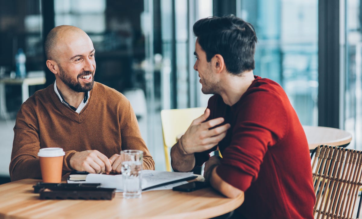Dos hombres conversan animadamente en cafetería, práctica de idiomas Berlitz.