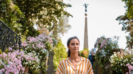 Una joven turista sostiene una cámara mientras sube una escalera exterior rodeada de flores.