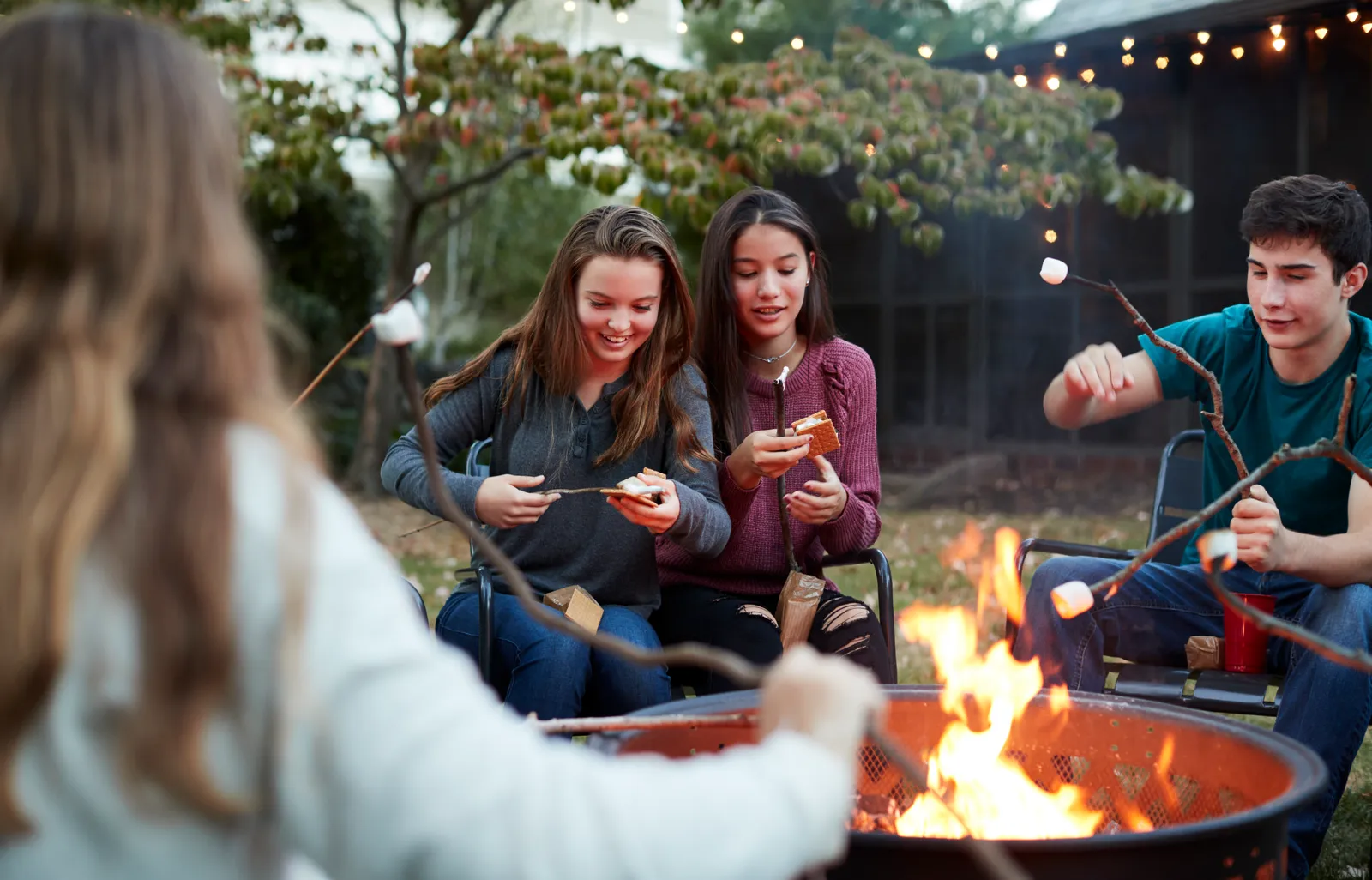 Adolescentes en un campamento, alrededor de una fogata en el patio.