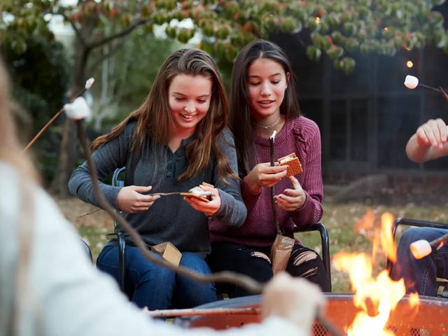 Adolescentes en un campamento, alrededor de una fogata en el patio.