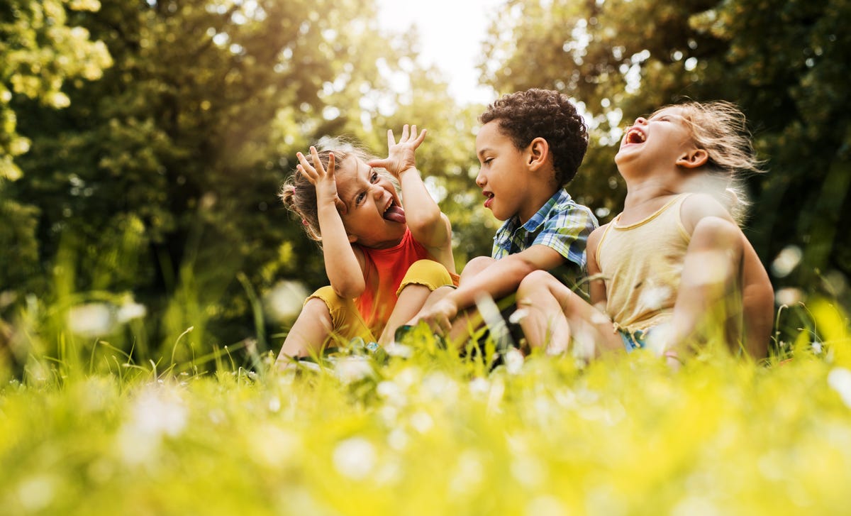 Tres niños se divierten y hacen caras graciosas en el pasto, disfrutando al aire libre.