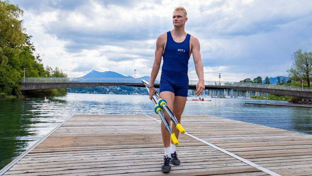 Rowing athlete walking on a dock carrying oars, illustrating preparation and discipline in competitive rowing.
