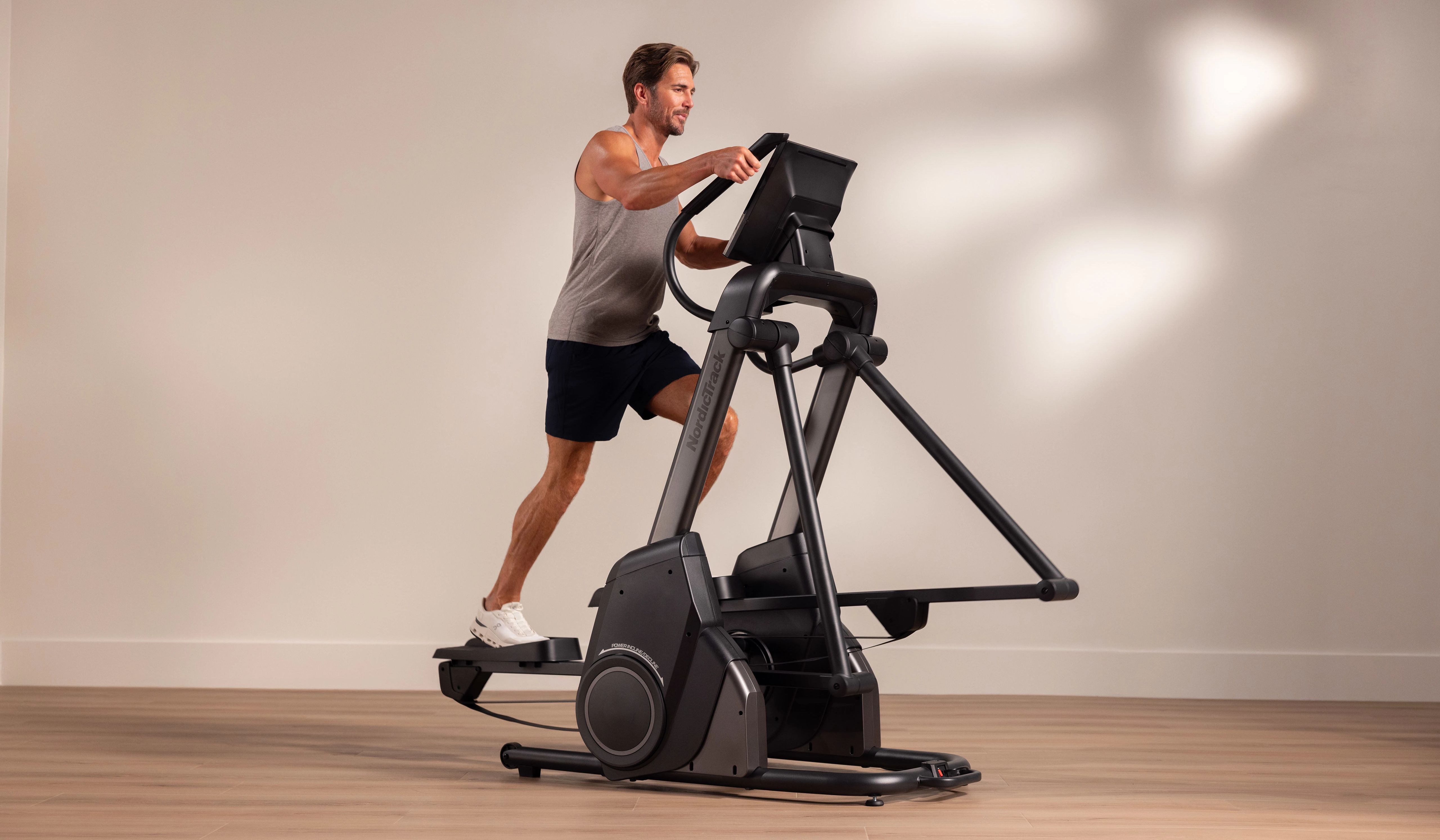 A man uses the NordicTrack X16 elliptical in a clean home setting, demonstrating the machine’s free-motion stride and upper-body engagement for a full-body cardio workout.
