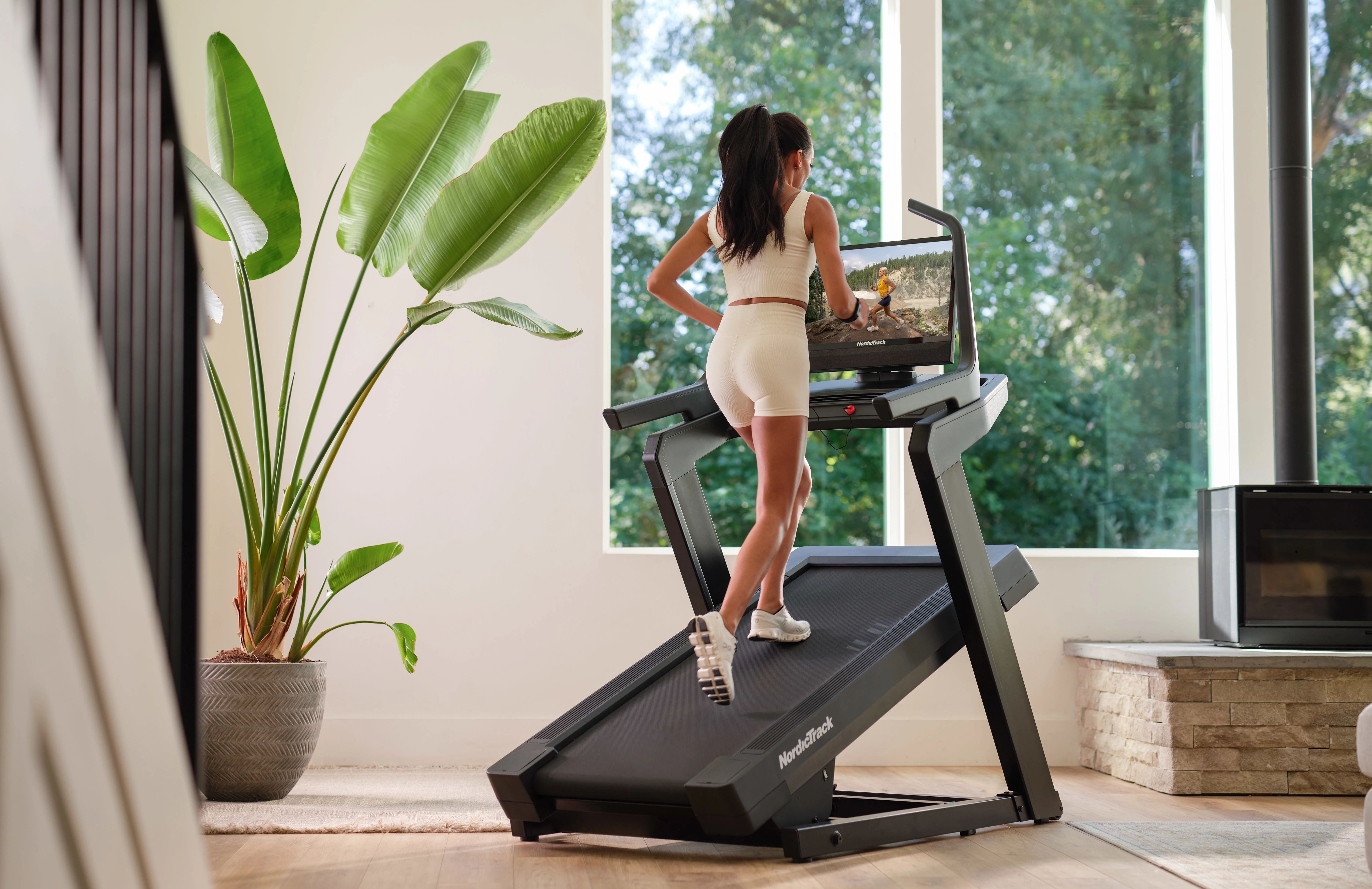 woman using NordicTrack smart treadmill with large screen during guided iFIT workout at home