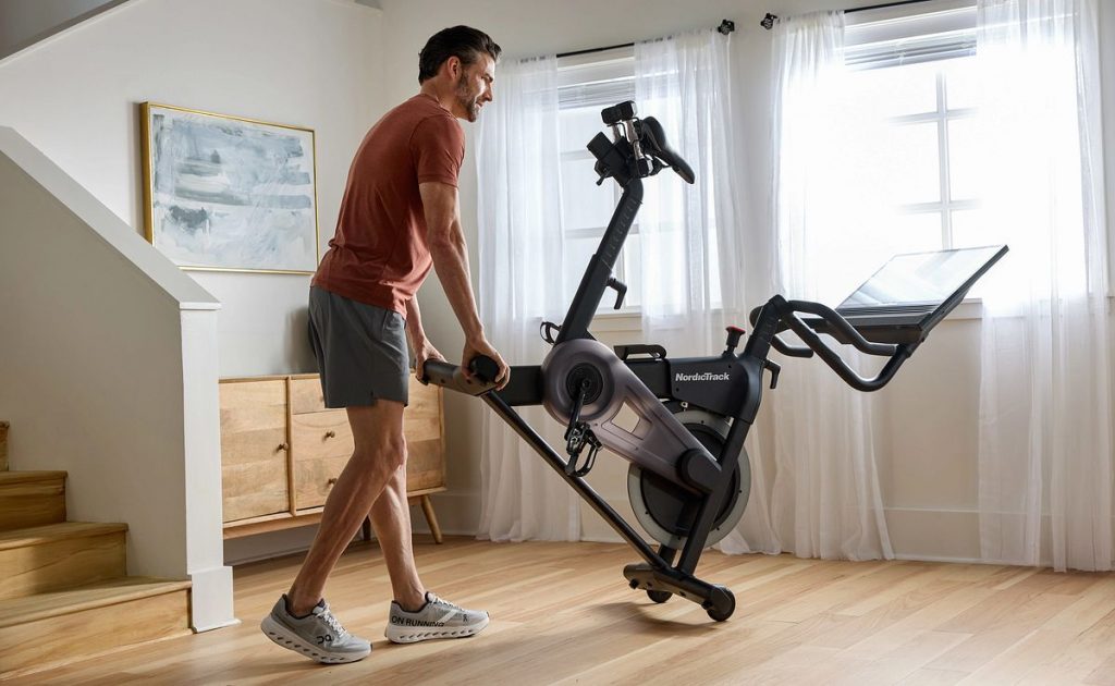Individual moving a NordicTrack exercise bike in a home space, demonstrating portability and space-conscious design.