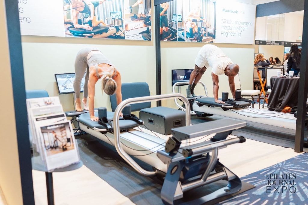 Attendees experiencing a live demonstration of connected reformer Pilates equipment at a fitness expo.