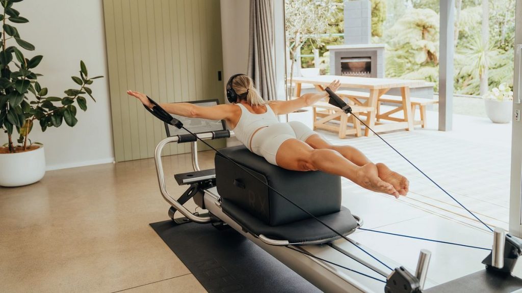 Individual performing a prone arm extension exercise on a Pilates reformer with resistance straps, highlighting posture and upper-body engagement.