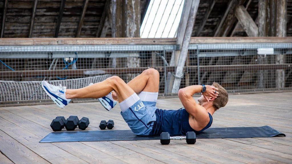 Athlete performing a core-focused strength exercise with dumbbells on a mat, representing accessible resistance training for muscle maintenance.