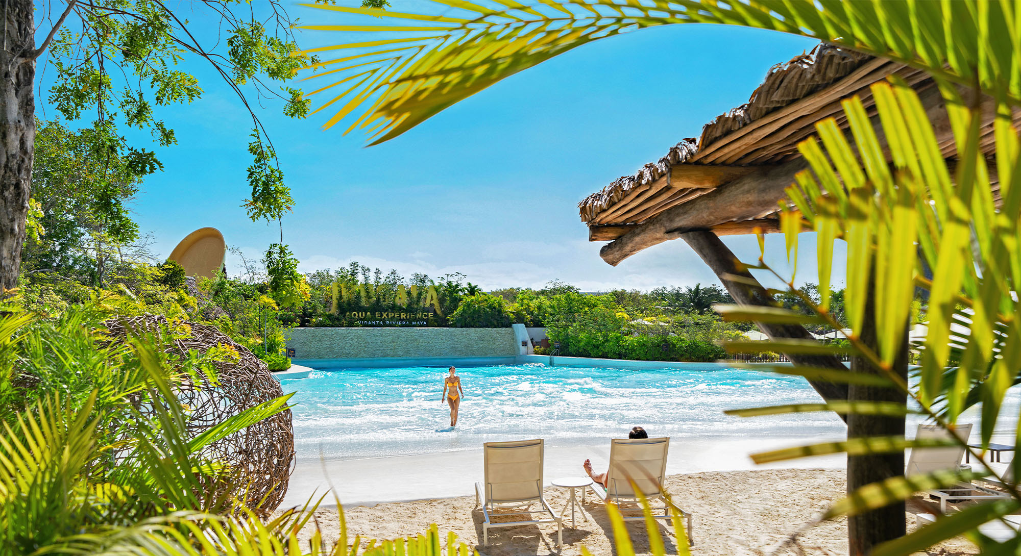 Wave pool at Jungala Aqua Experience water park with a sandy beach entry, palapa and lounge chairs surrounded by jungle