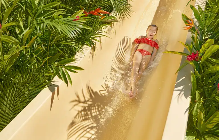 Niña deslizándose por un tobogán infantil en Jungala Aqua Experience, rodeada de vegetación tropical