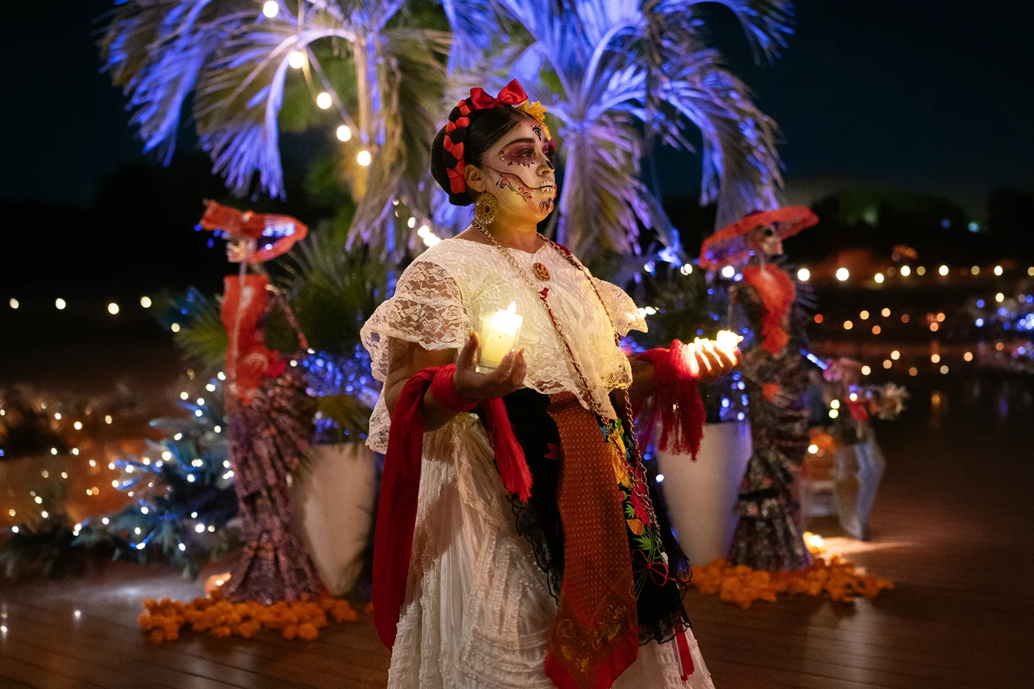 Woman in Catrina makeup and traditional dress holding candles